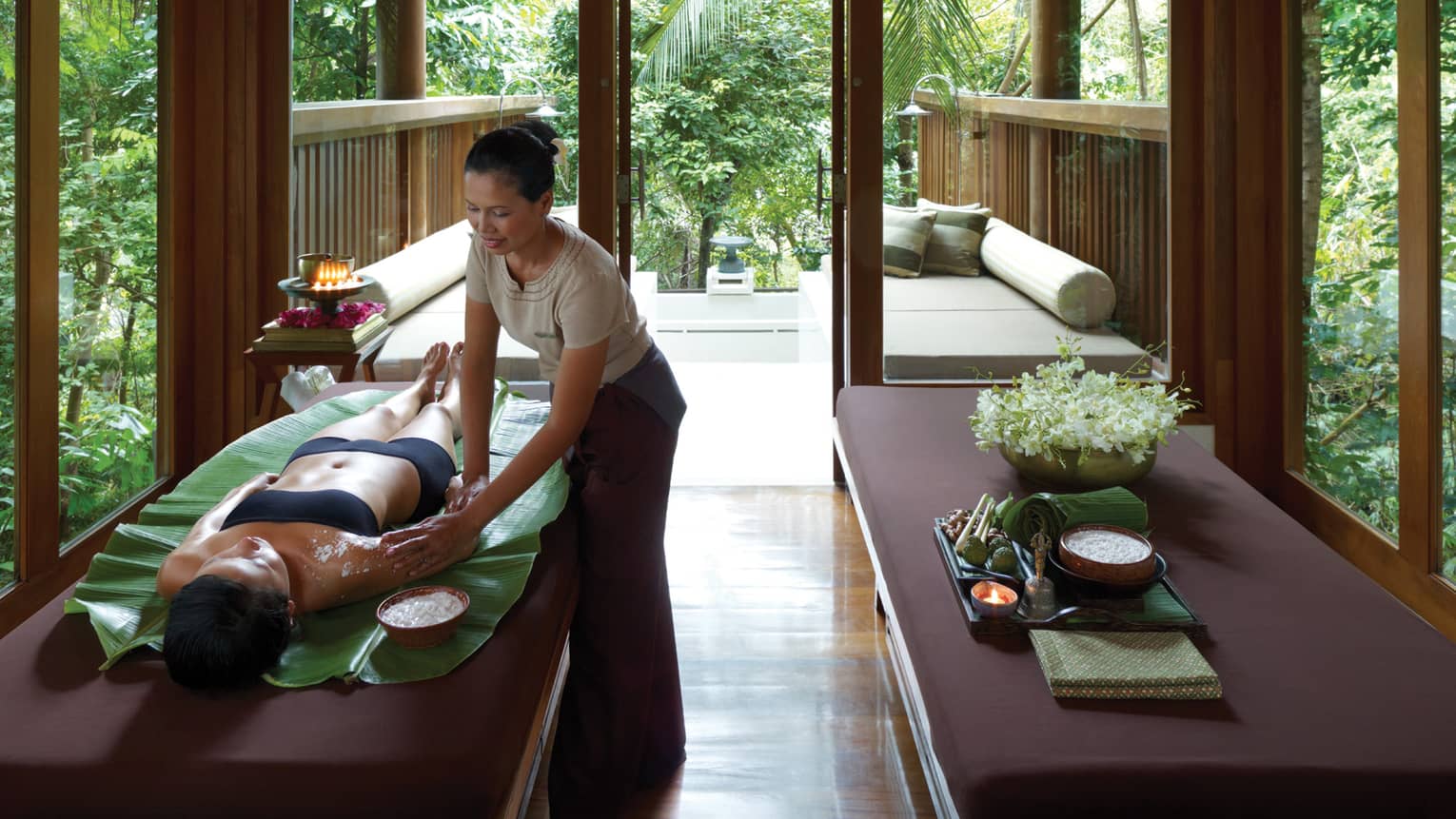 Woman getting massage, salt scrub in wood Garden Spa Pavilion with candles