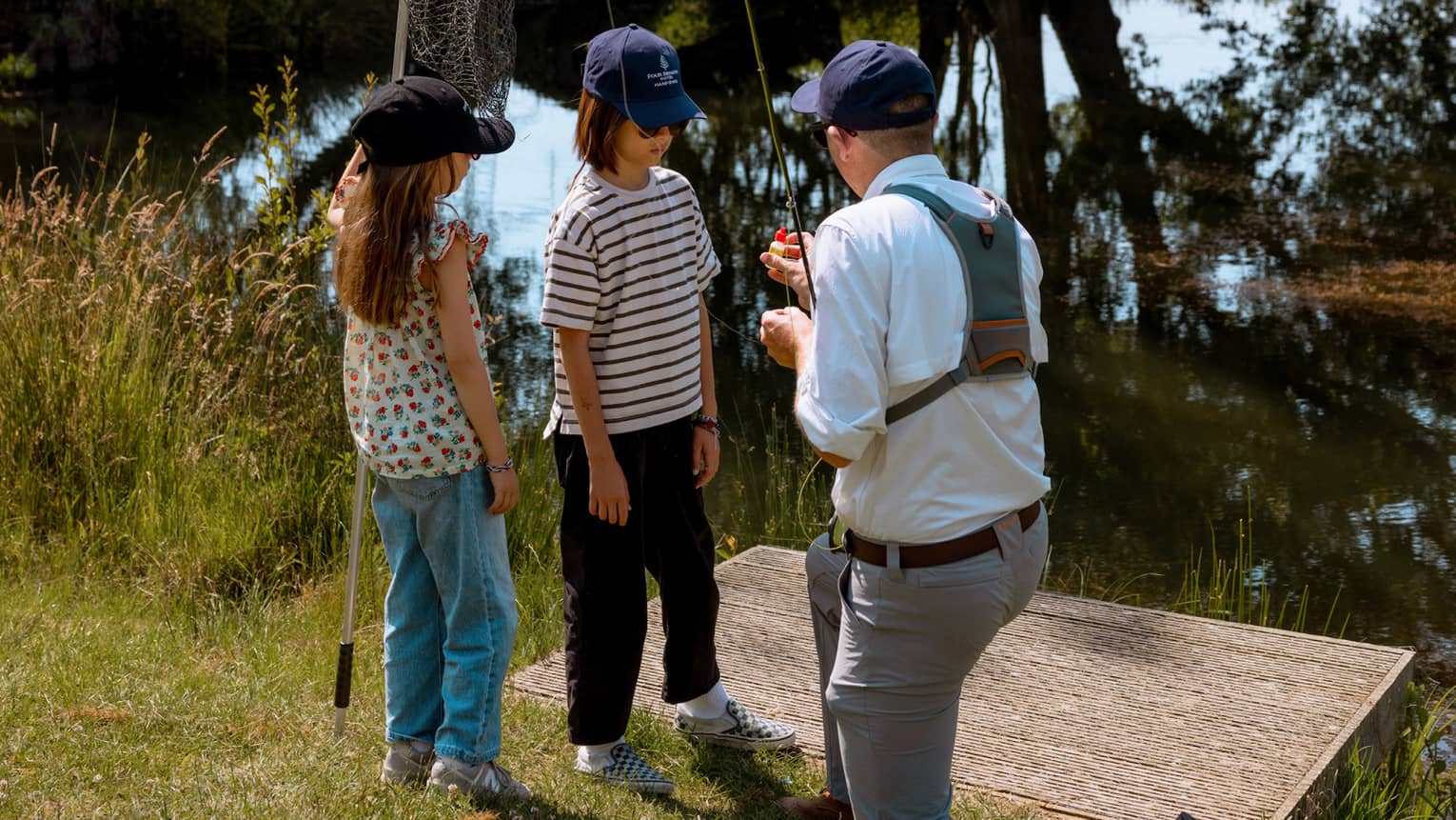 Fishing instructor holding fishing rod and kneeling in front of two children with one holding a net