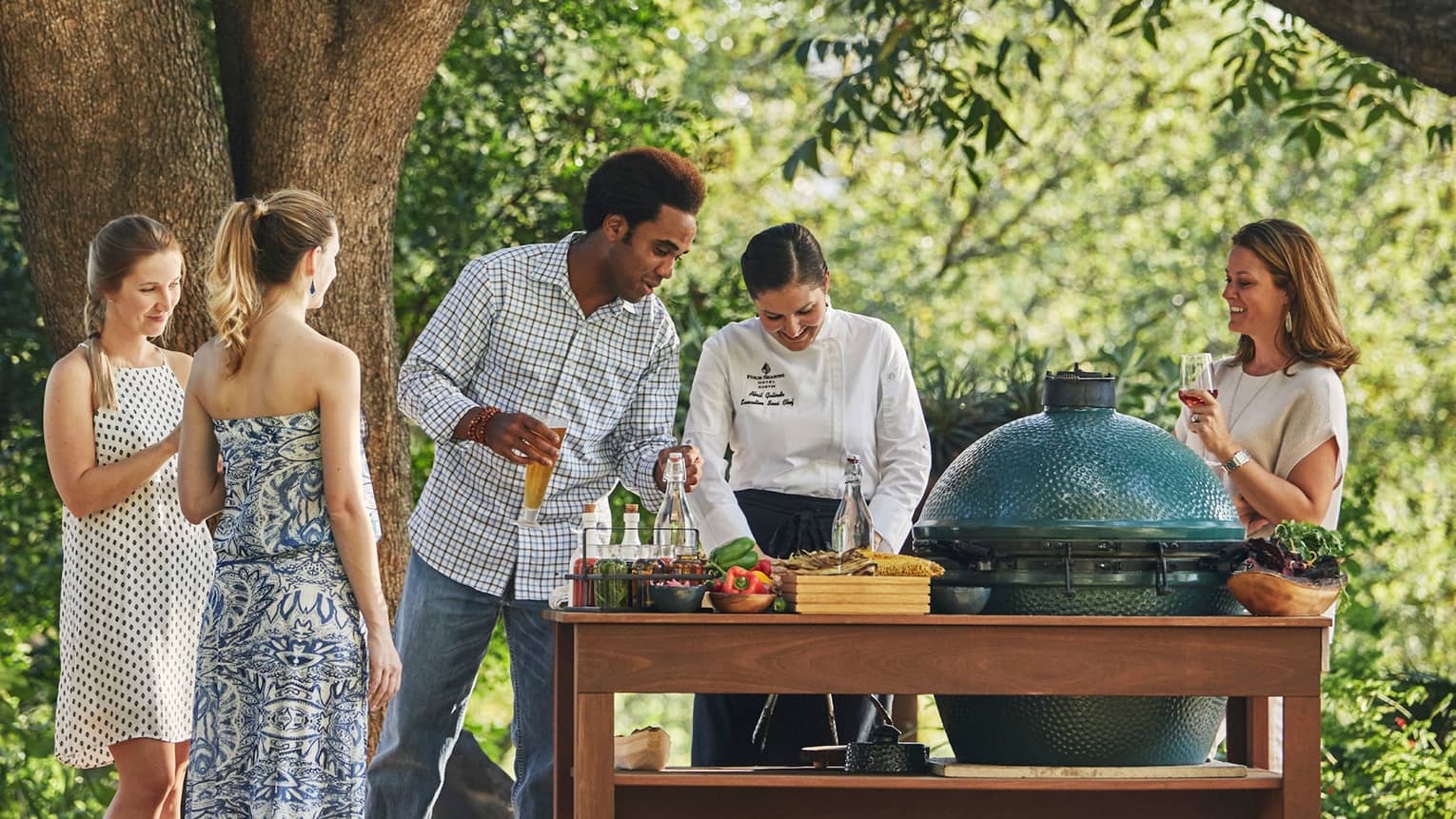 Group of friends watch as chef prepares meal at outdoor garden barbecue