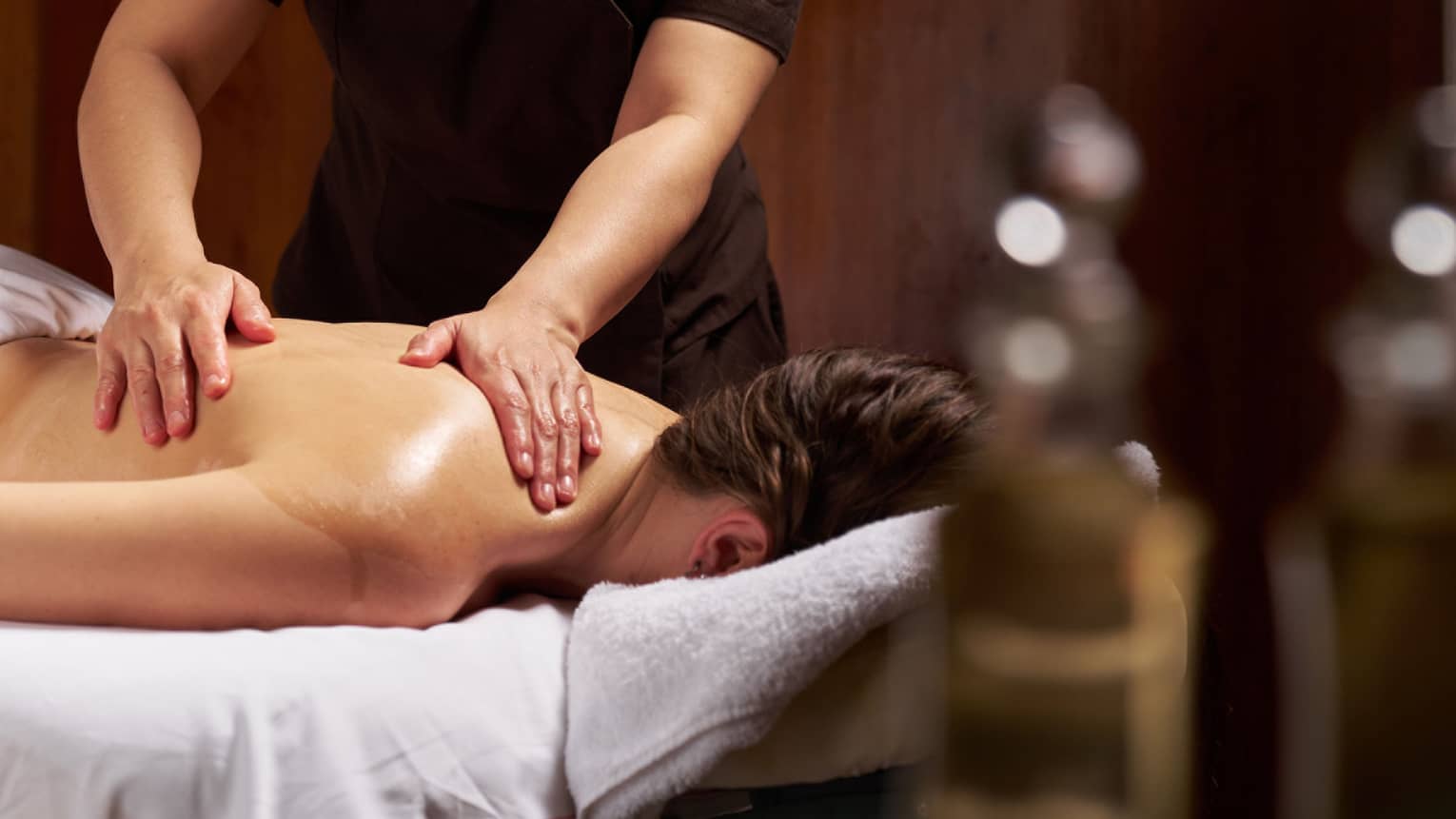 Masseuse performs treatment on female guest lying face down on massage table