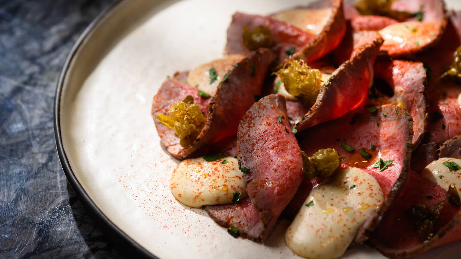 Thinly sliced rare beef and tuna sauce, all dusted with paprika, on round white plate