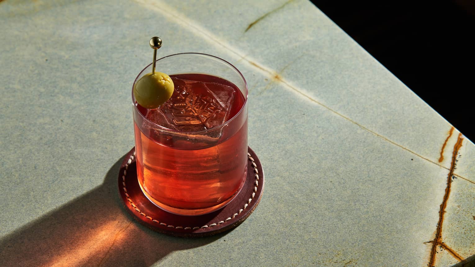Red-coloured cocktail in a rocks glass garnished with a green olive