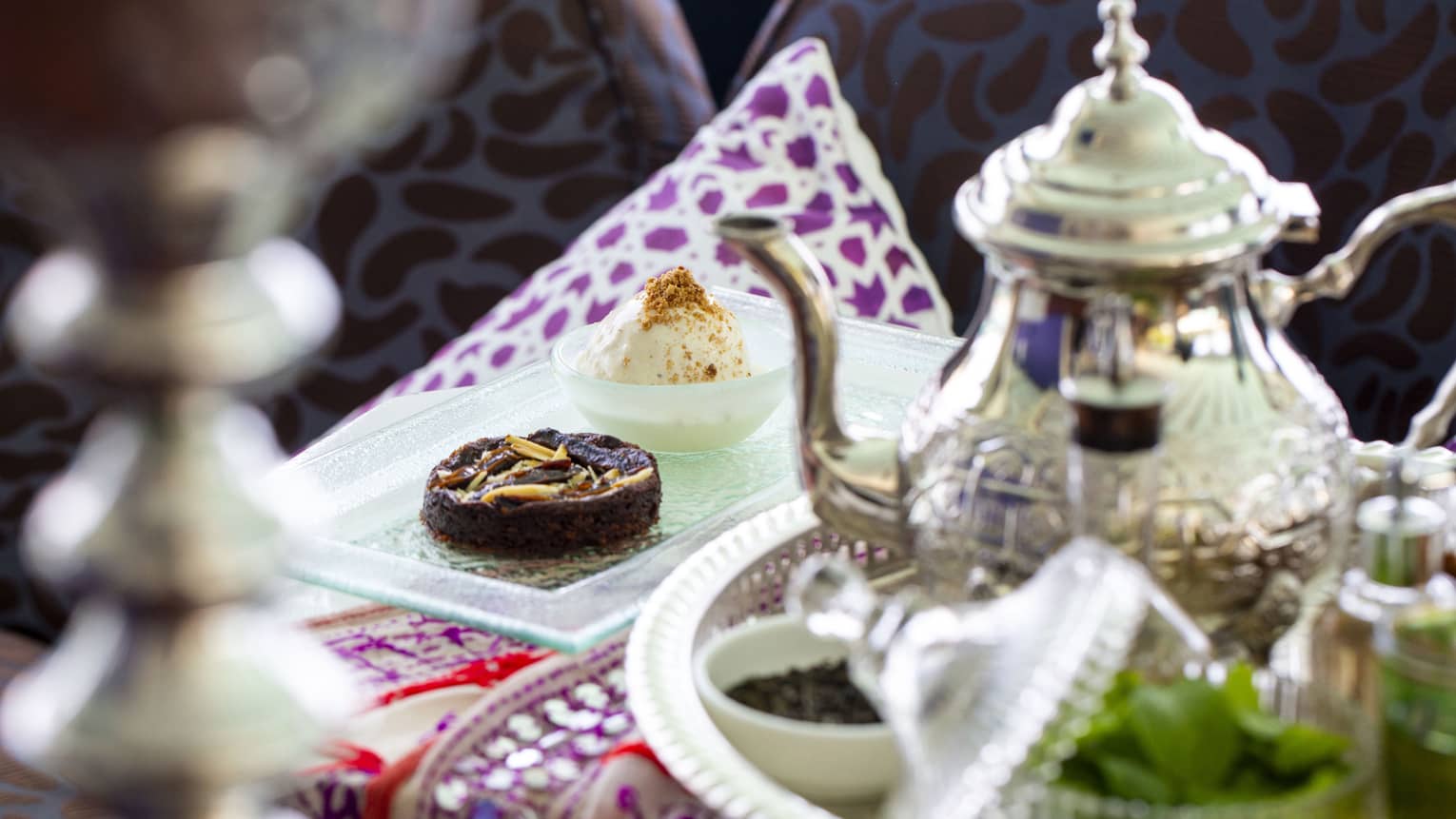 A sterling silver teapot and light tea time finger foods sit on a decorative table spread atAl Barakat