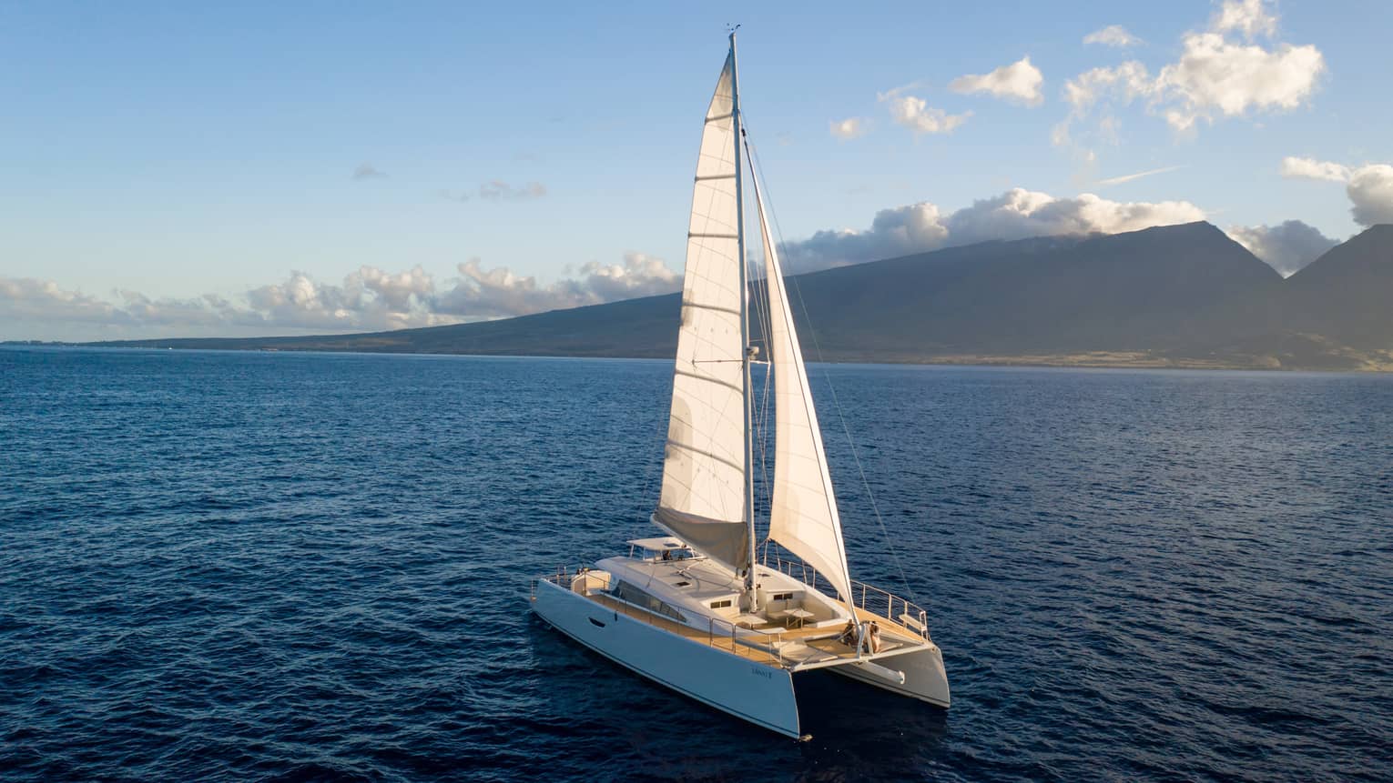 Catamaran sailing on the open water against a mountain backdrop