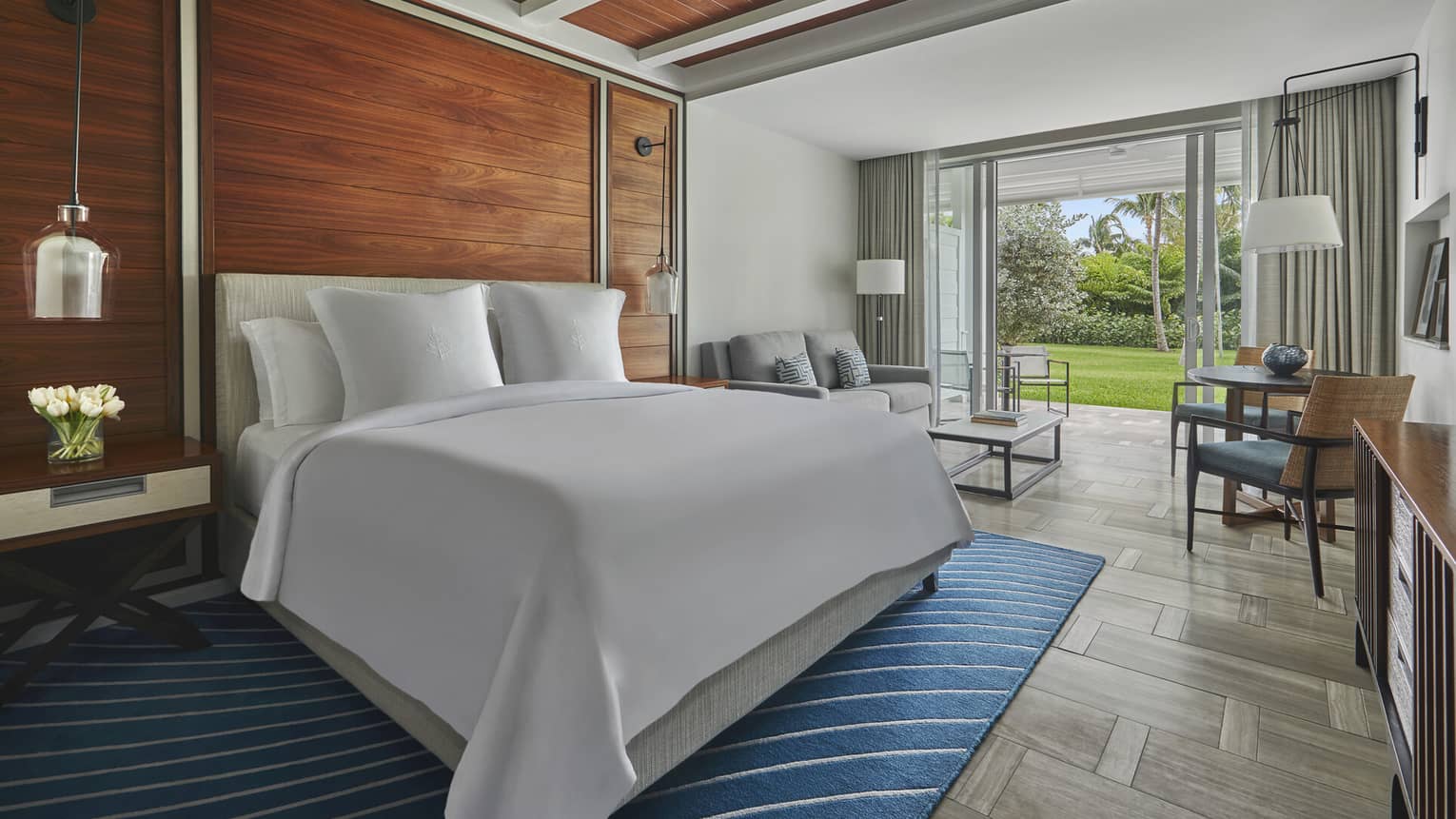 Room with a king-size bed, wooden accent wall and large glass doors opening to a green garden patio area at a Four Seasons luxury resort