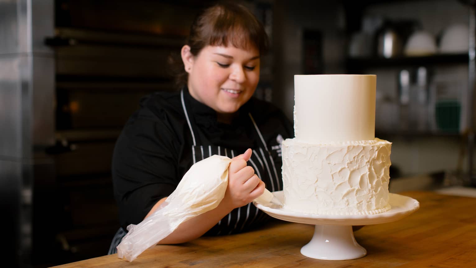 Pastry chef decorates two tiered wedding cake on stand