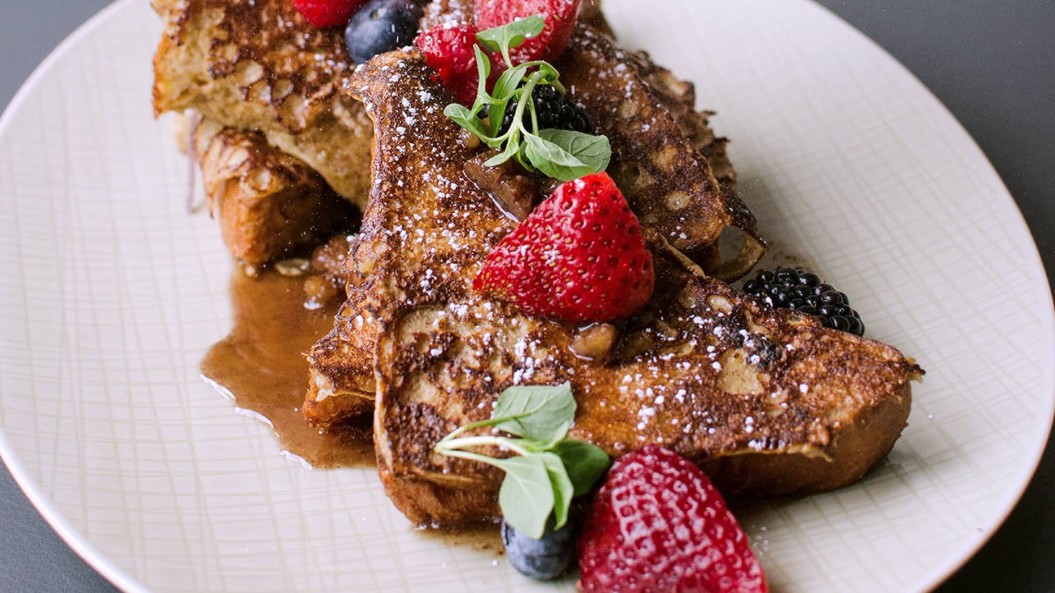 French toast topped with fresh berries, greens, syrup on white plate