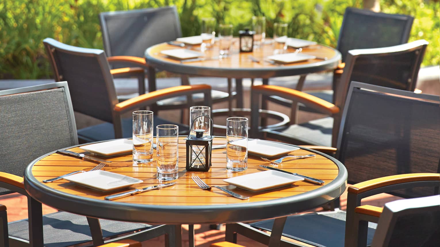 Round patio tables set with plates, glasses, lanterns on sunny day