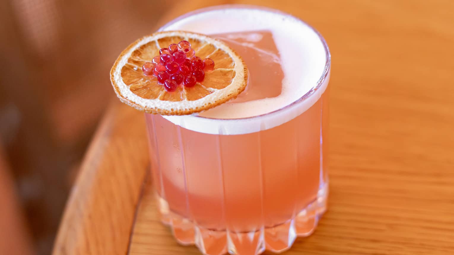 Coral-hued cocktail served in a rocks glass and garnished with an orange slice