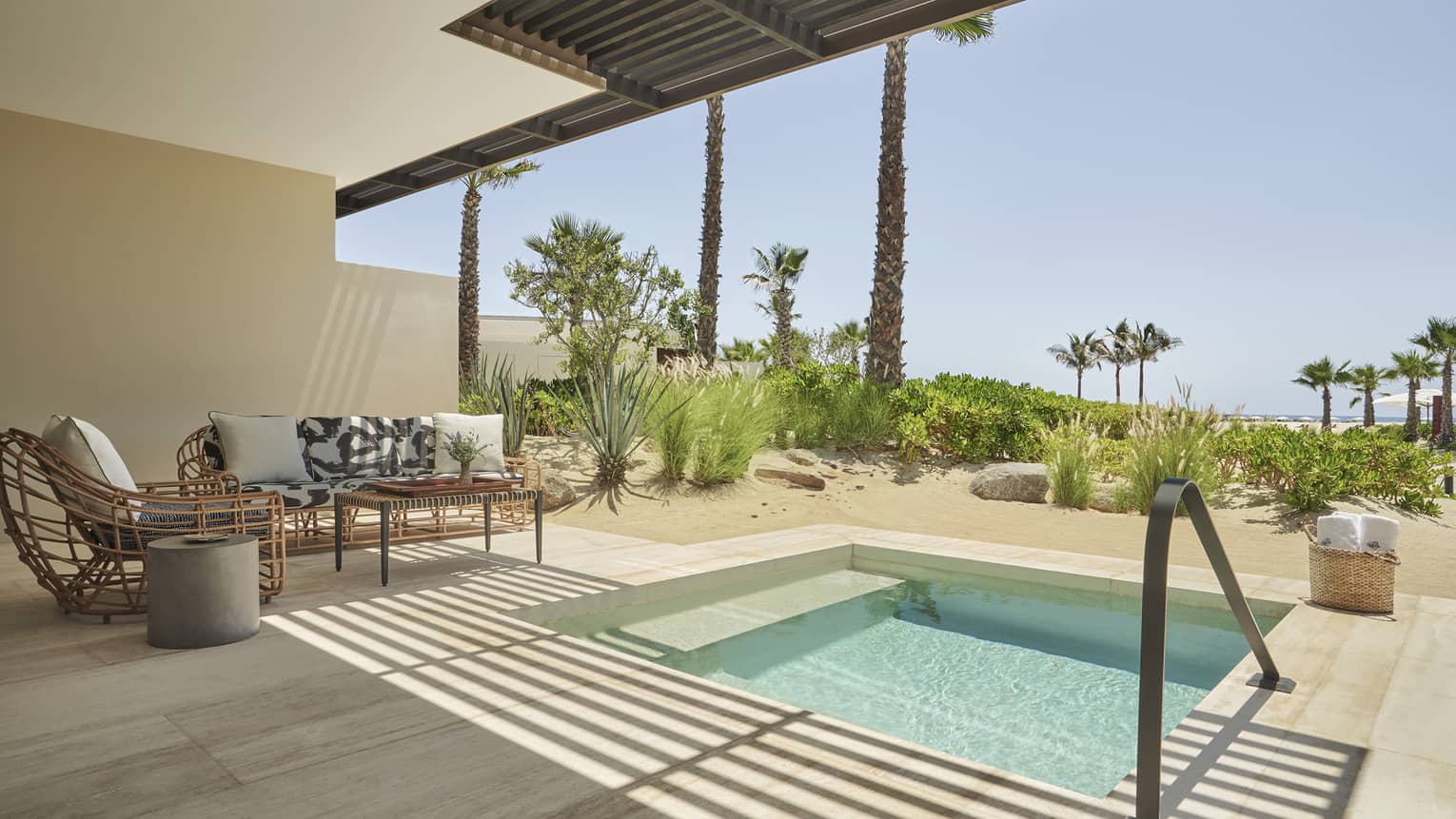 A plunge pool outside in the sun next to a sofa and chair.