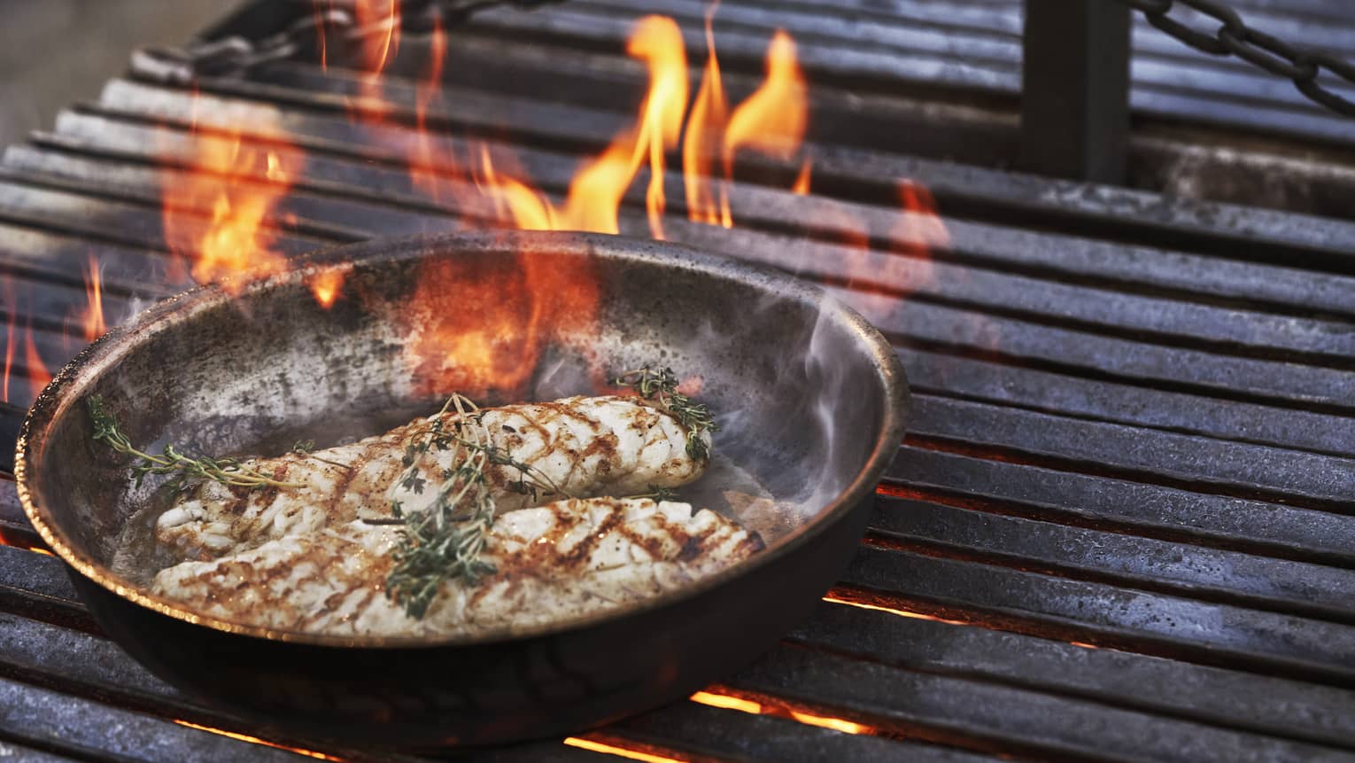 Meat cooking on a fire grill in a round and flat pan.
