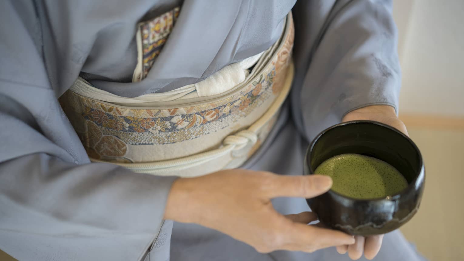 Close-up of woman in blue robe holding bowl with green matcha tea