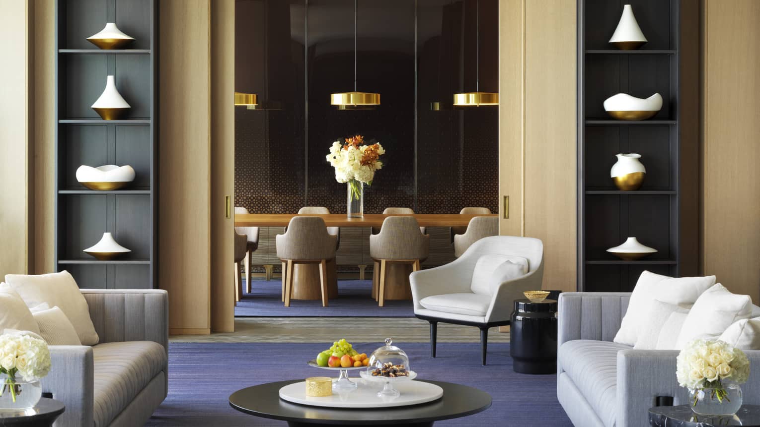 Modern dining table, gold lamps in private room behind lounge with tall bookshelves, sofas