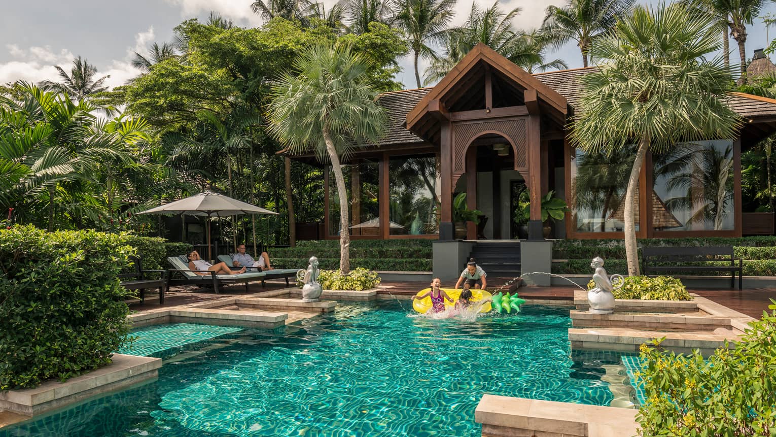 Family swims under monkey fountains in private residence outdoor swimming pool