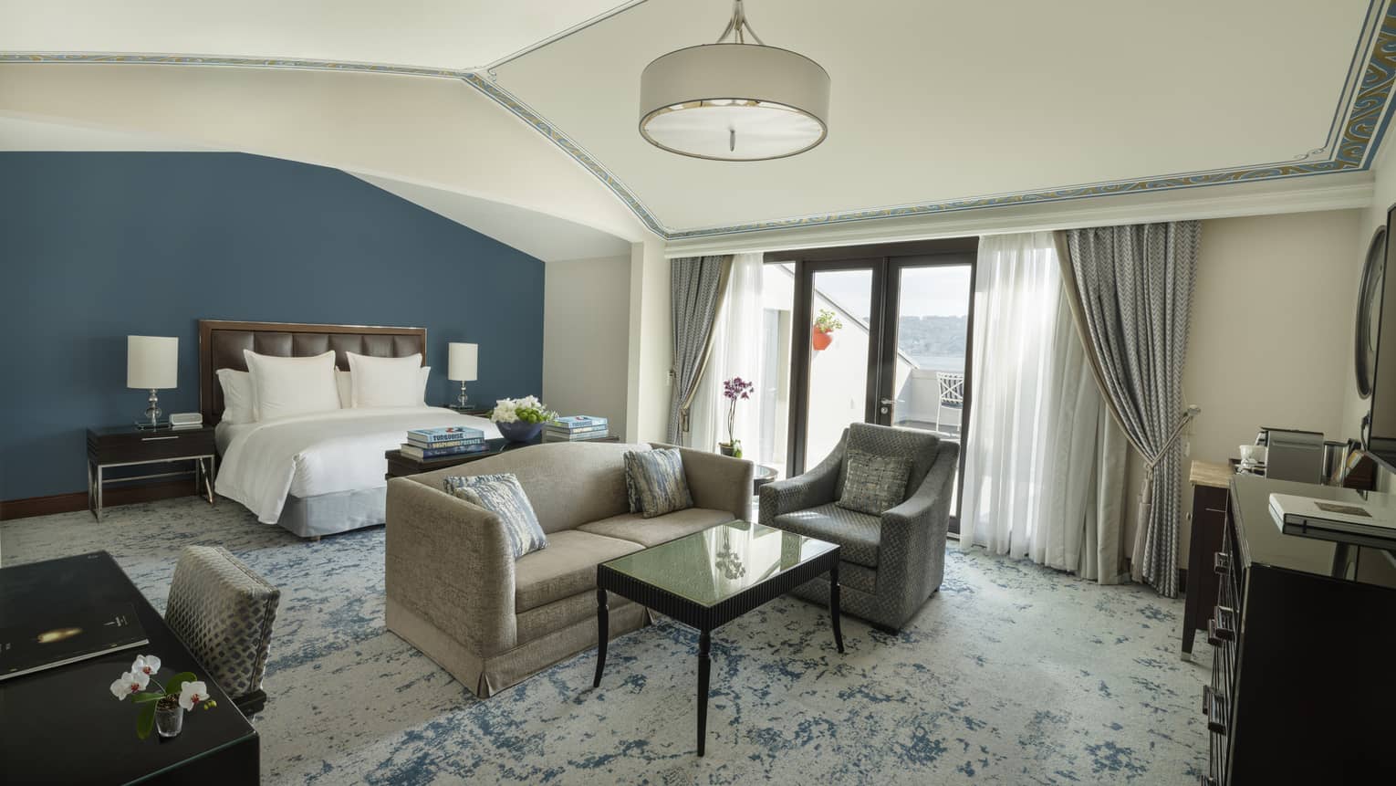 Elegant hotel suite featuring a king bed and sitting area with a sofa, arm chair and coffee table, plus a walk-out rooftop terrace