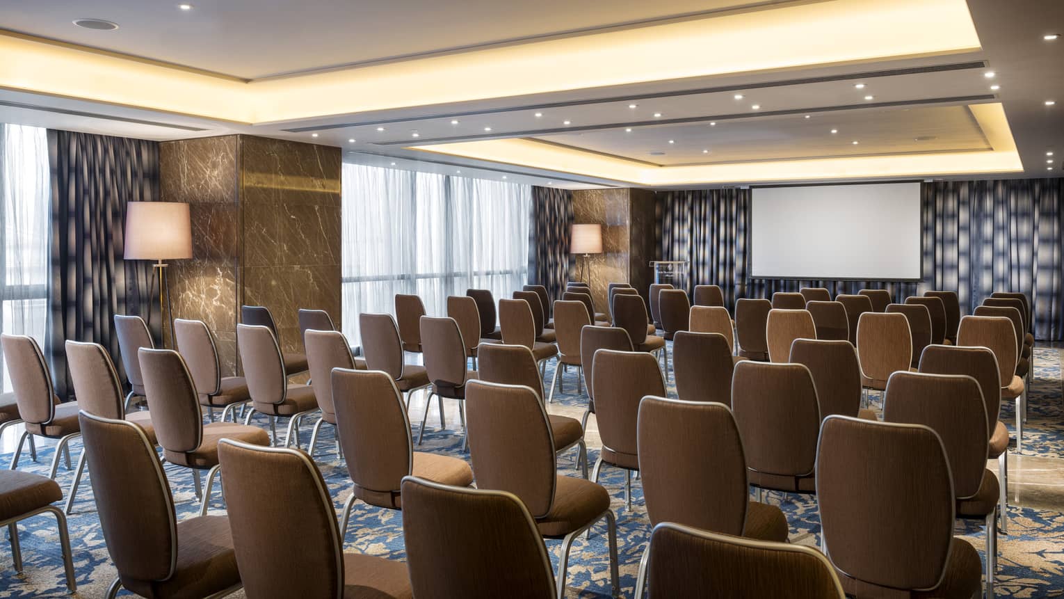 Rows of chairs facing screen in large meeting room with marble pillars
