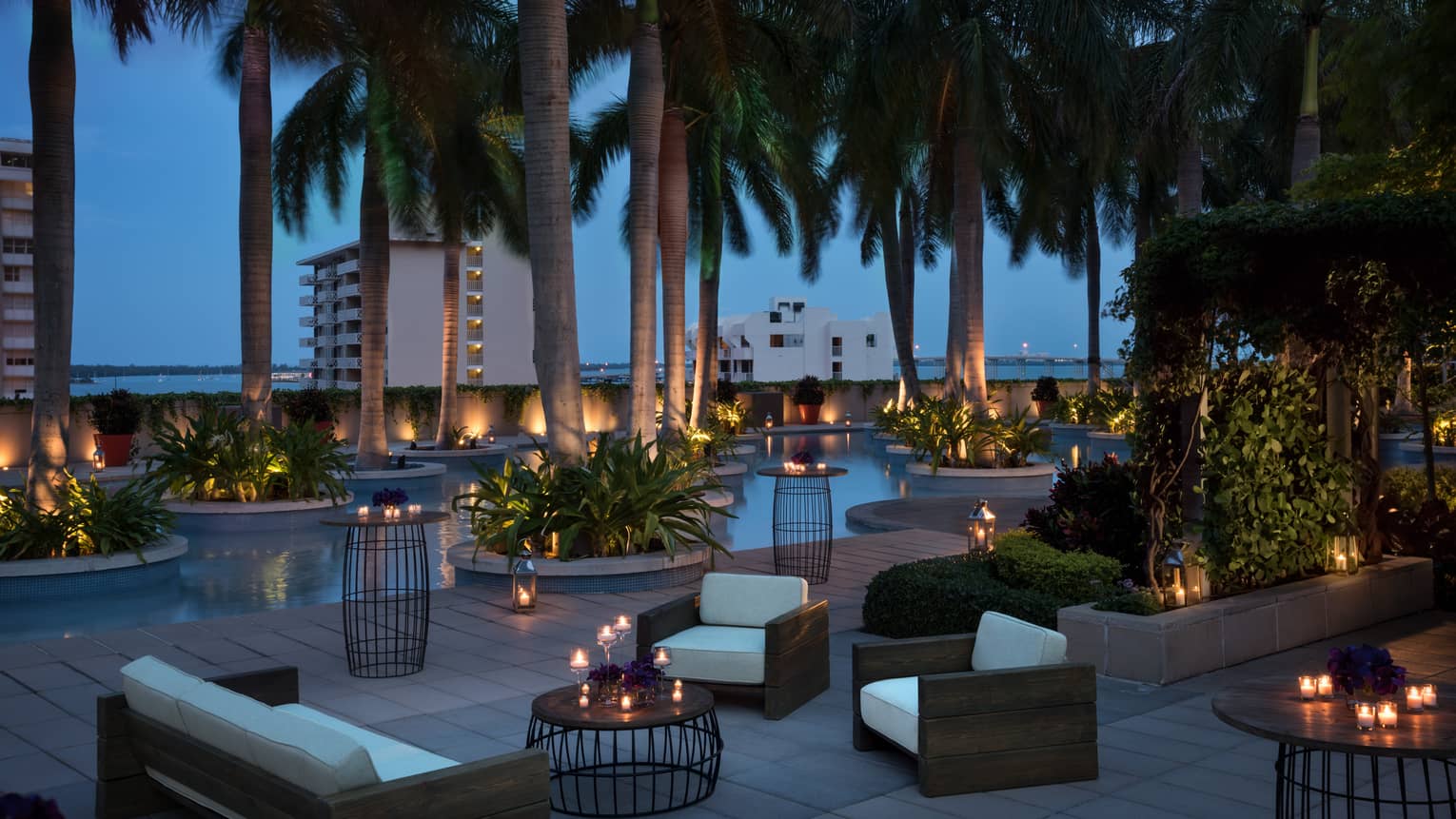 Plush white patio sofas and chairs, candle-lit tables under palm trees at night