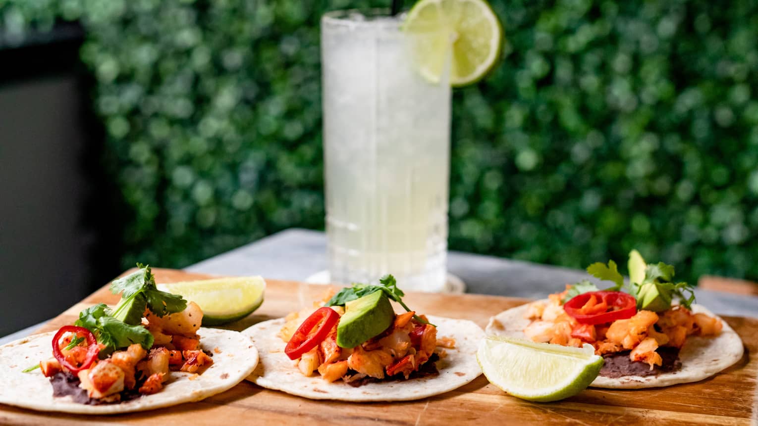 Three tacos and a clear drink on a wooden tray.