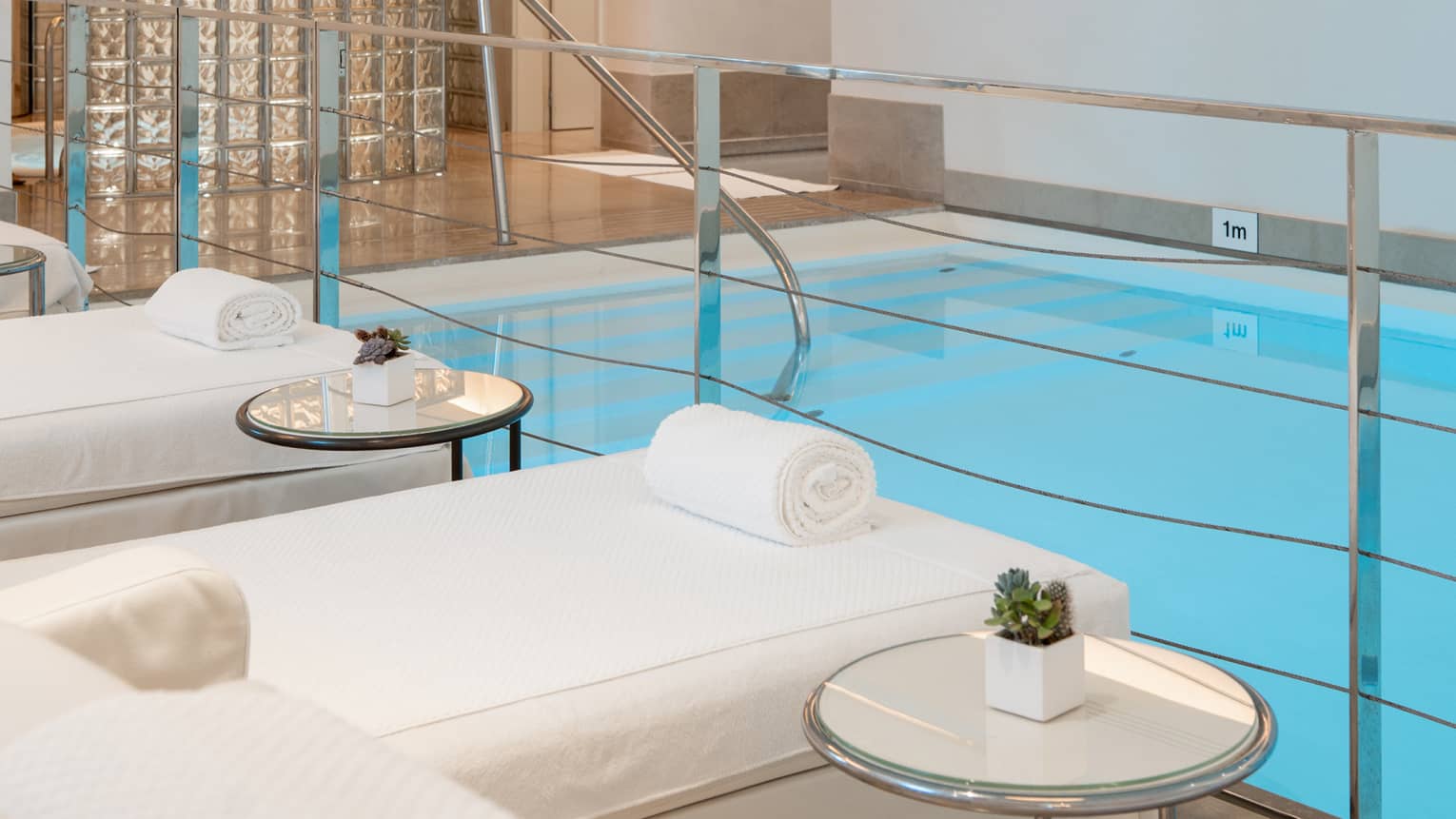 A spacious, well-lit indoor pool area with comfortable poolside spa treatment tables