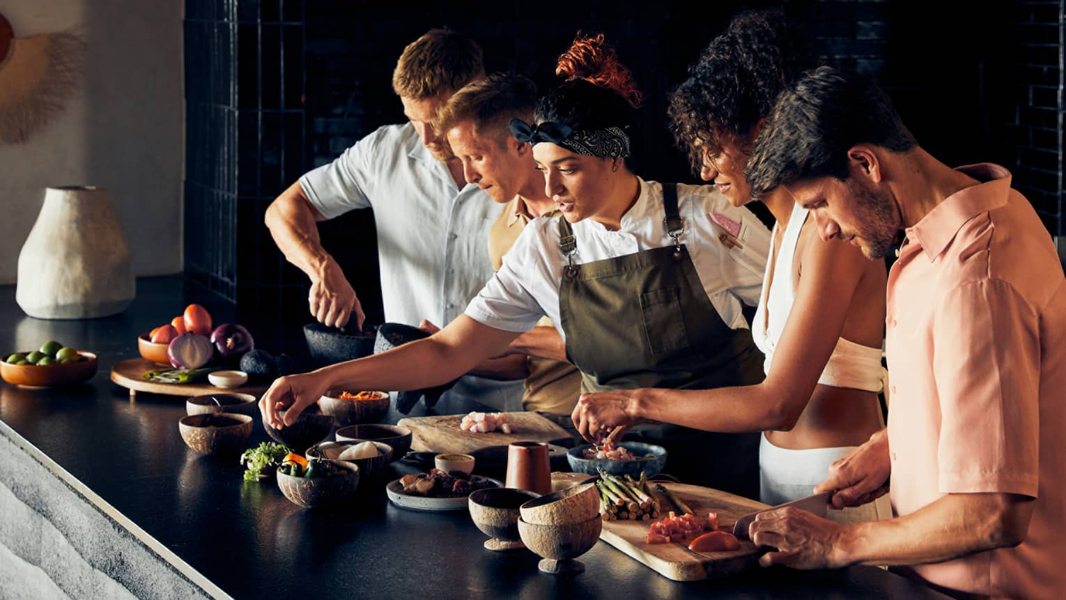 A group of people and a chef cooking food on a black counter.