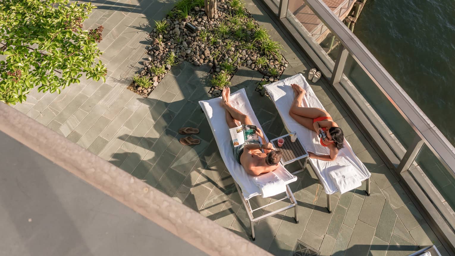 A couple relaxing on pool loungers on a terrace overlooking a water view