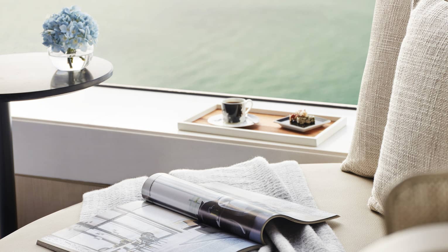 Magazine and blanket set on a lounge chair, next to window looking out to harbour