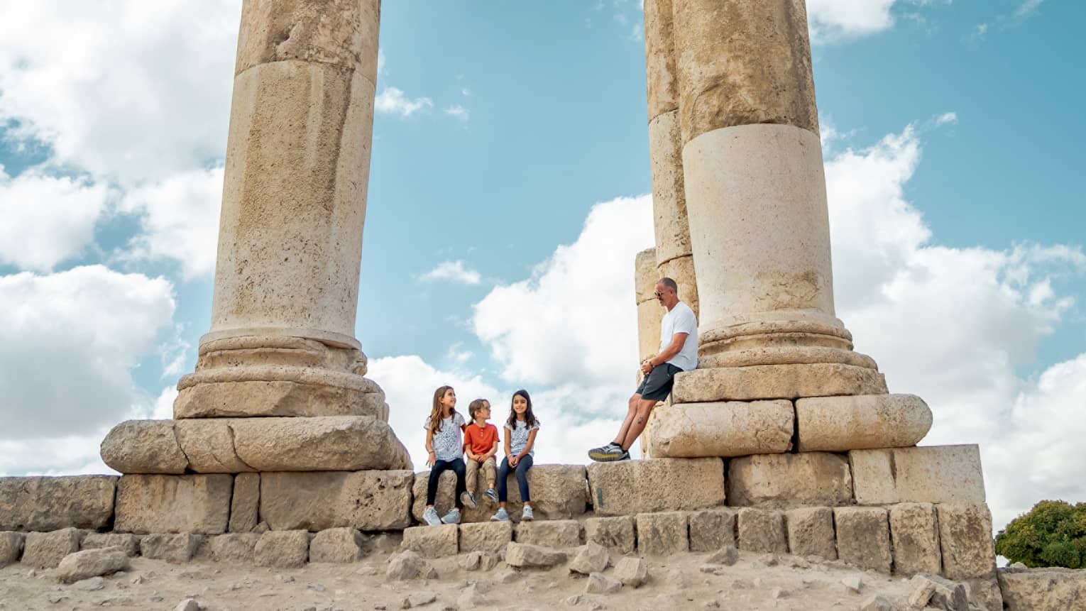 A family sitting in the center of a set of stone pillars in front of a blue sky.