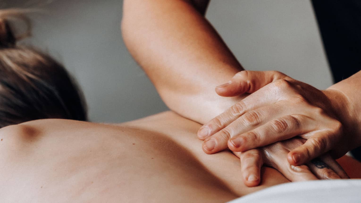 Massage therapists rubs a person's bare back with one hand placed on top of the other