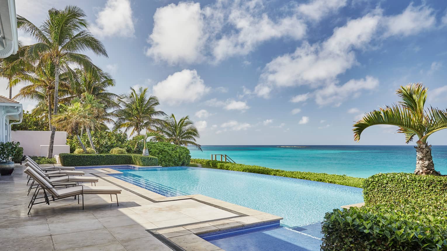 Lounge chairs on deck by outdoor swimming pool, ocean and blue sky