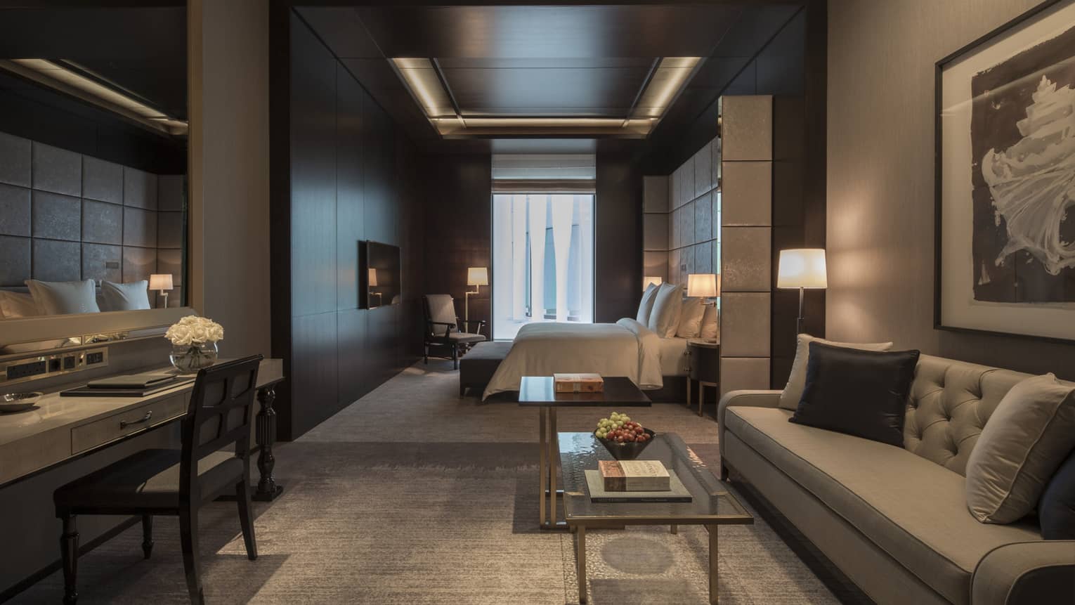 Executive room living area with full-size grey sofa and desk, bedroom in background