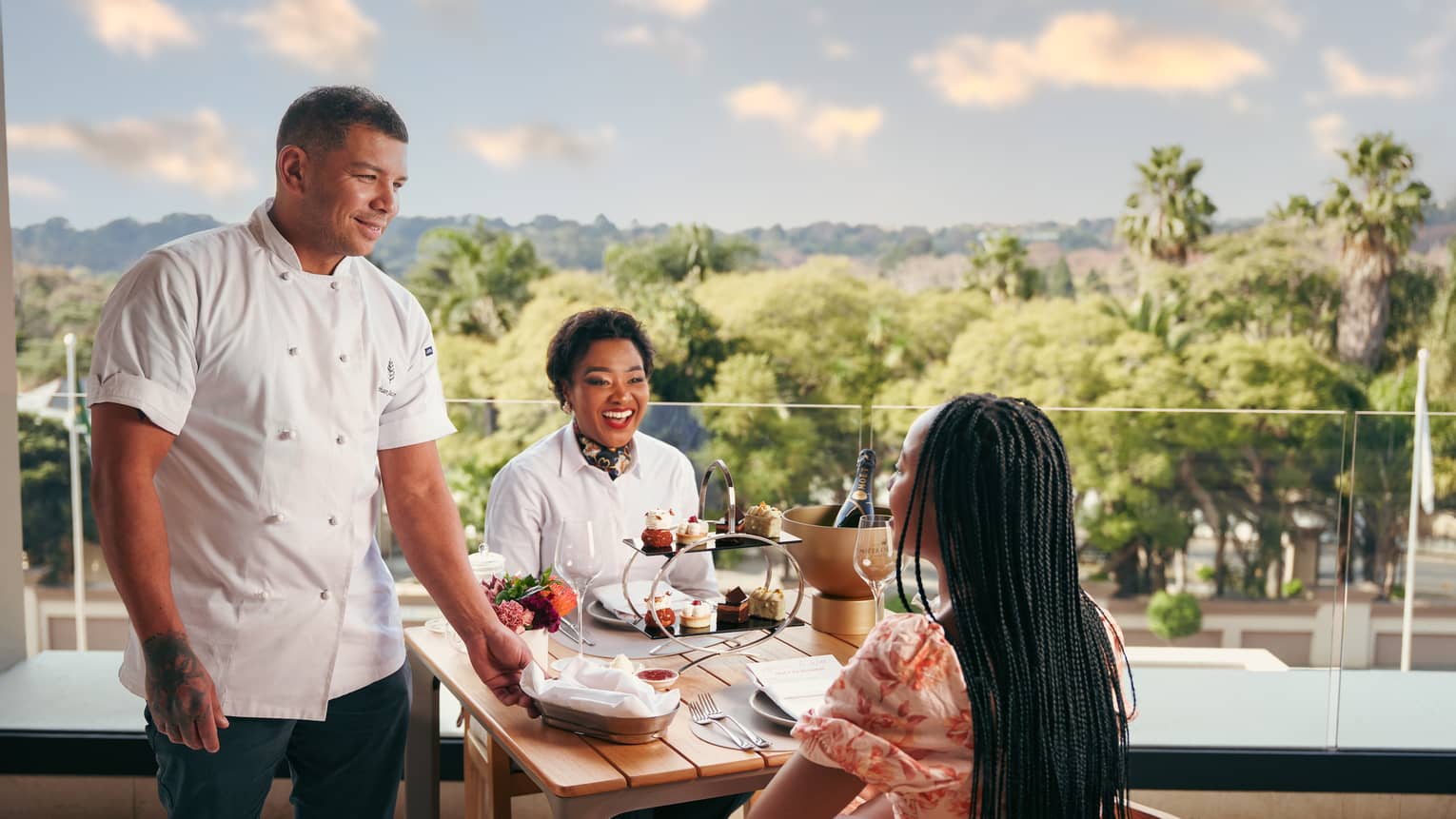 A chef visits a table where two women sit enjoying afternoon tea, with garden view