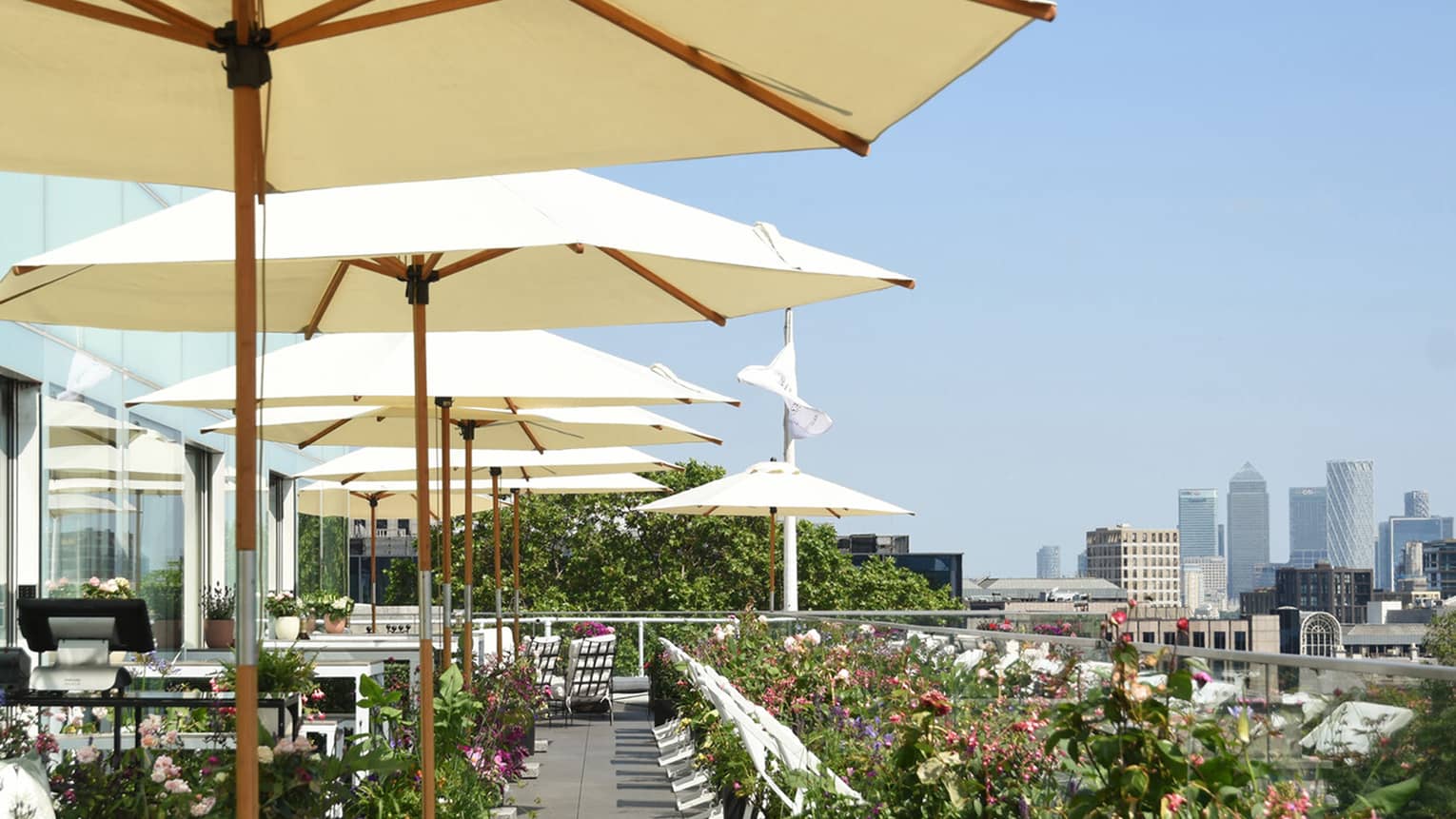A sunlit patio filled with umbrellas, dining tables and colorful florals overlooking the city