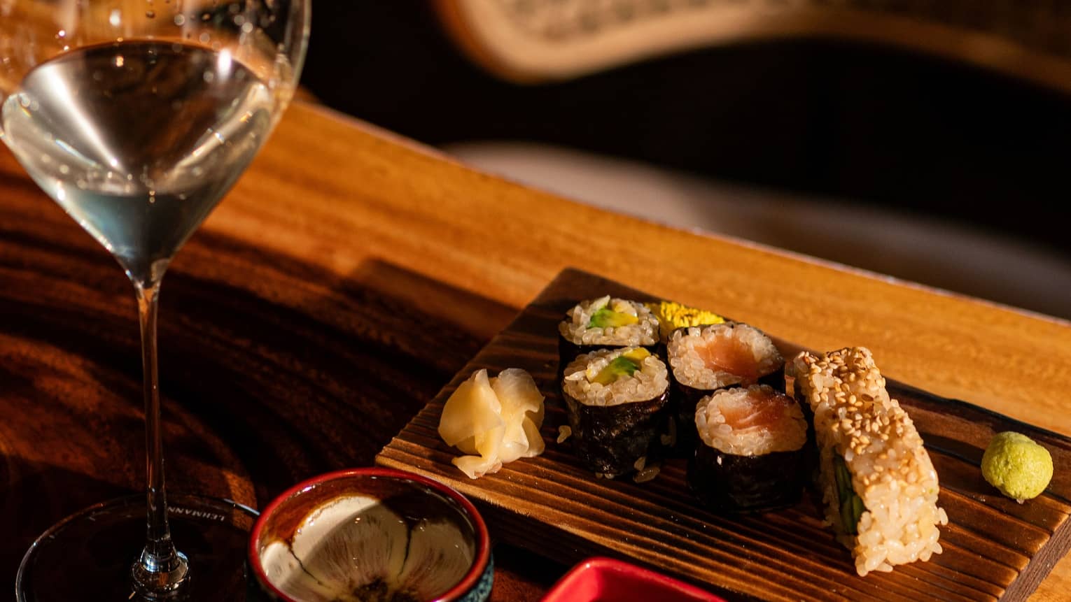 A glass of sake paired with sushi served on a wooden plate with decorate ceramic bowls