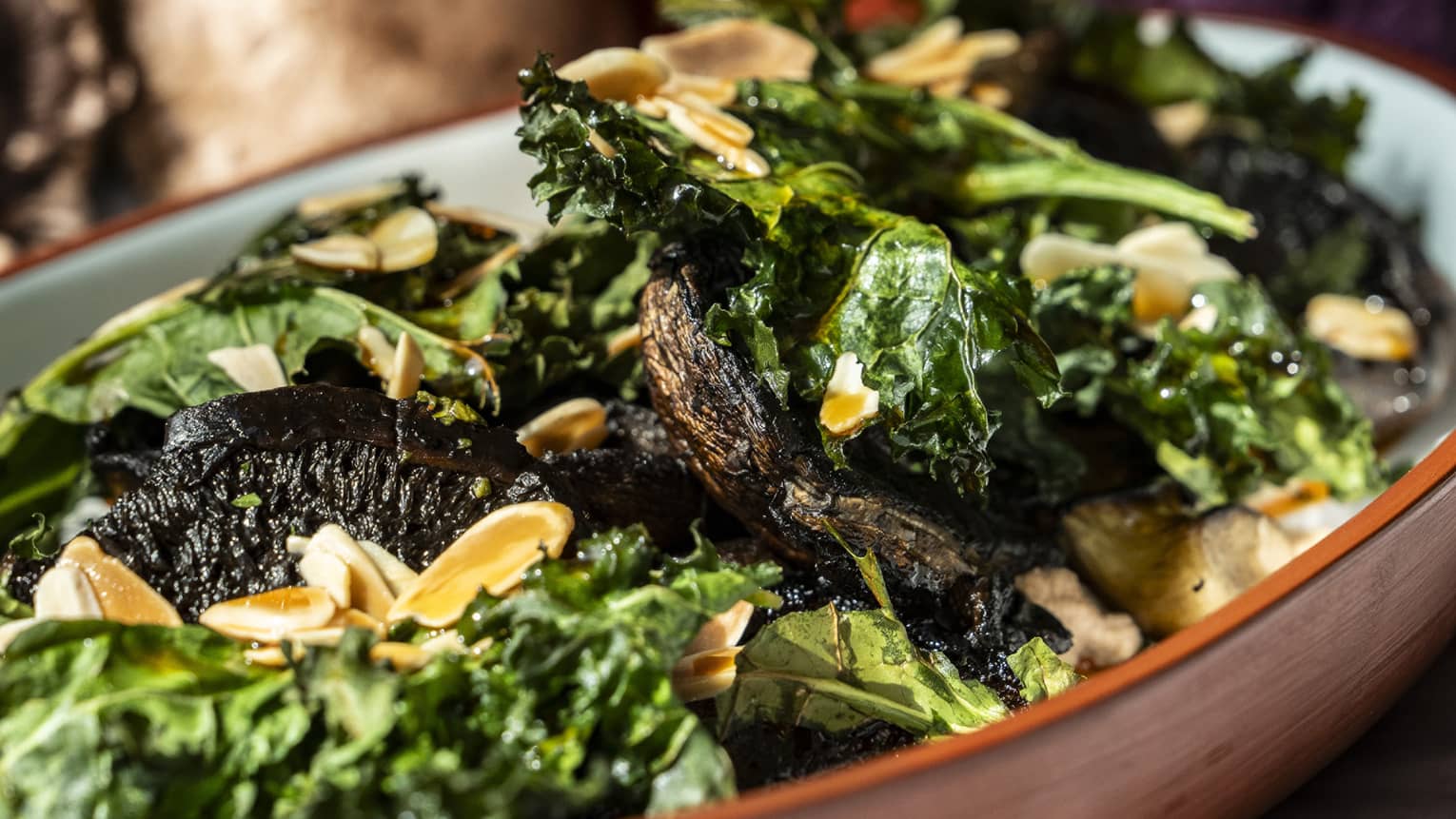 Grilled mushrooms with creamy almonds and kale chips served in an red oval serving platter