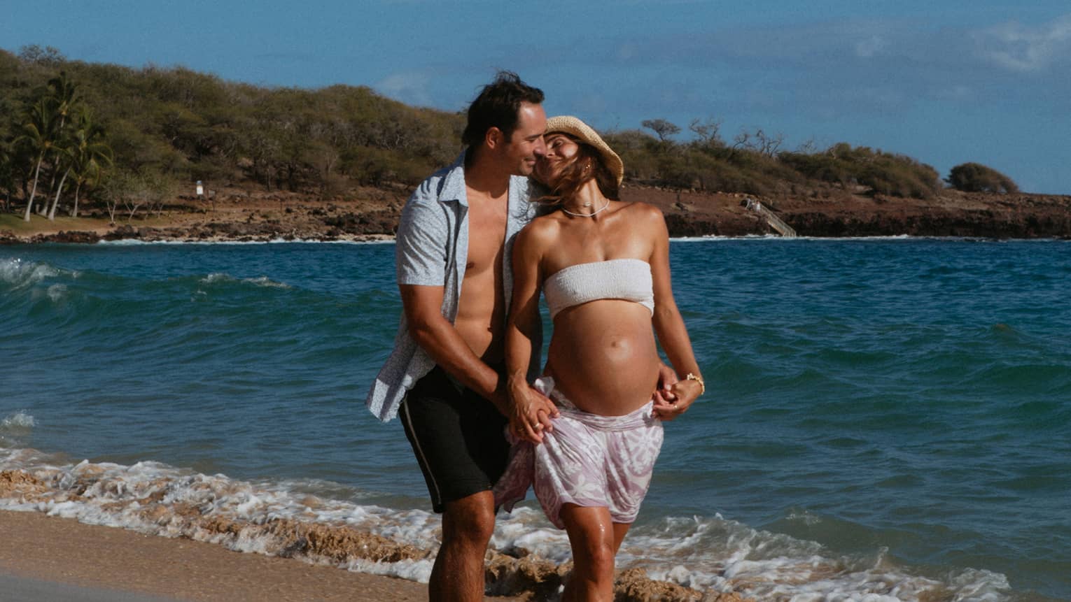 Man and pregnant woman walk together and embrace on the beach
