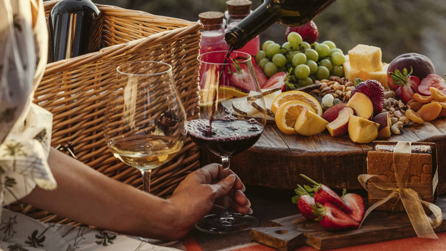 Guest eating a picnic outside with wine glasses and a fruit spread.