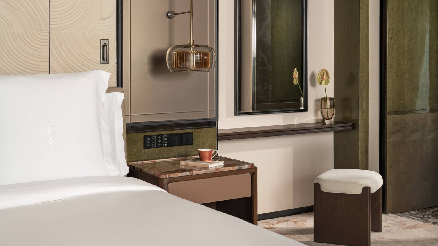 Hotel room detail of a cushioned stool next to a king bed and nightstand