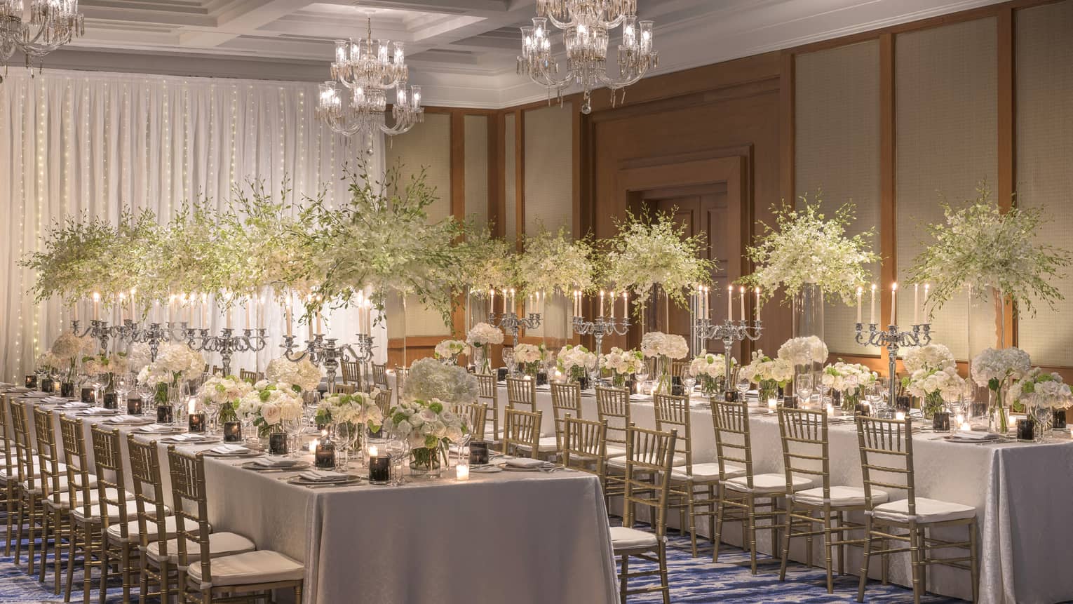 Two long tables are adorned with candelabras and tall and short bouquets of white flowers