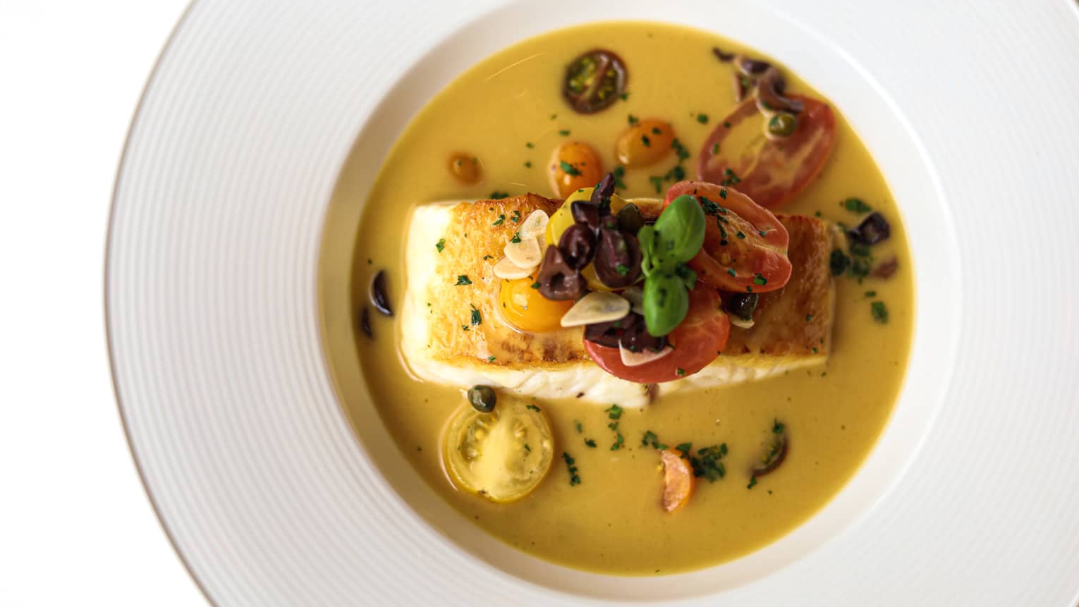 Seabass fillet, capers, olives, cherry tomatoes, white wine and butter served in a white wide-rimmed bowl