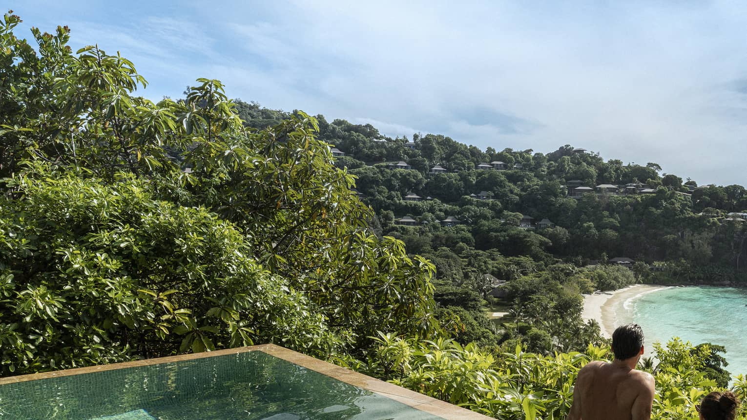 A couple looks out at a view of crystal blue waters and cliffs from an infinity pool