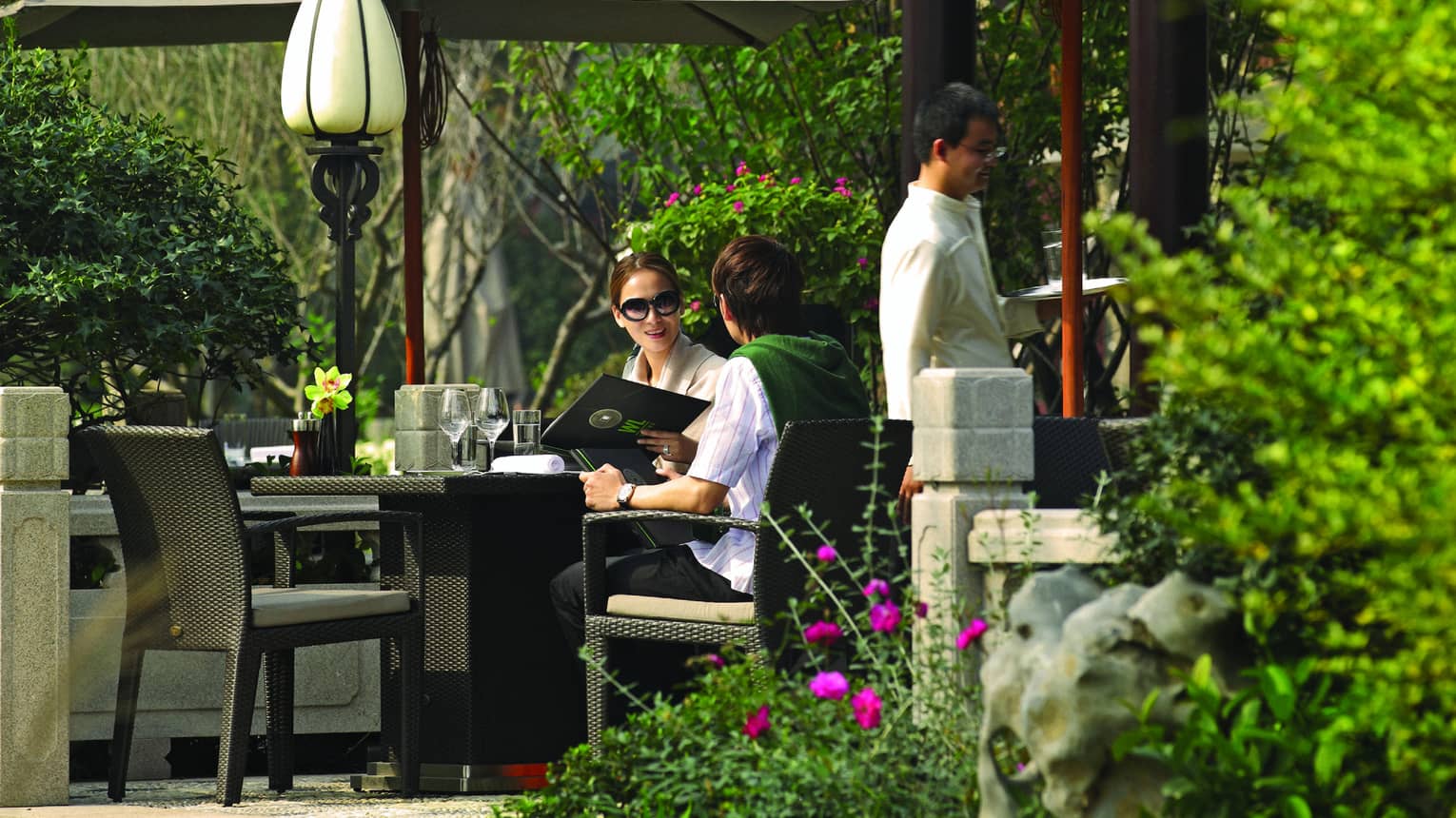 Couple holds menu at patio dining table under umbrellas, pavilion