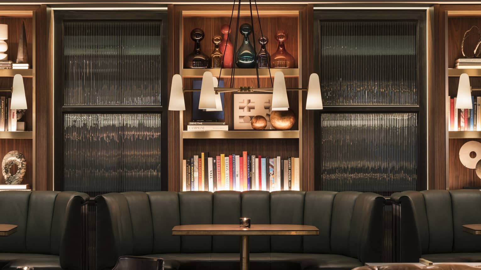A dining area with large black booths, book shelves and hanging lights.