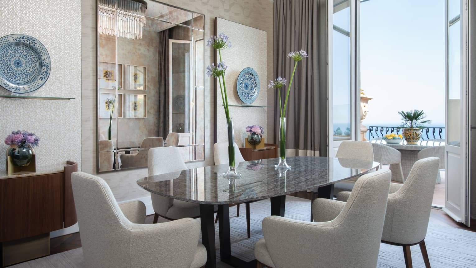 Dining table and six white upholstered chairs, doors opening to sea--view balcony