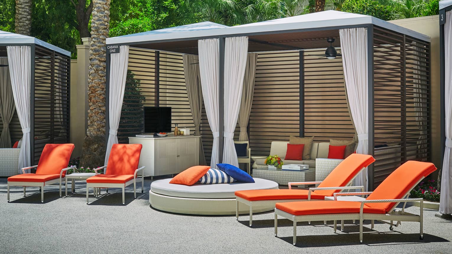Orange deck chairs, large plush ottoman by poolside cabana with sofas, TV