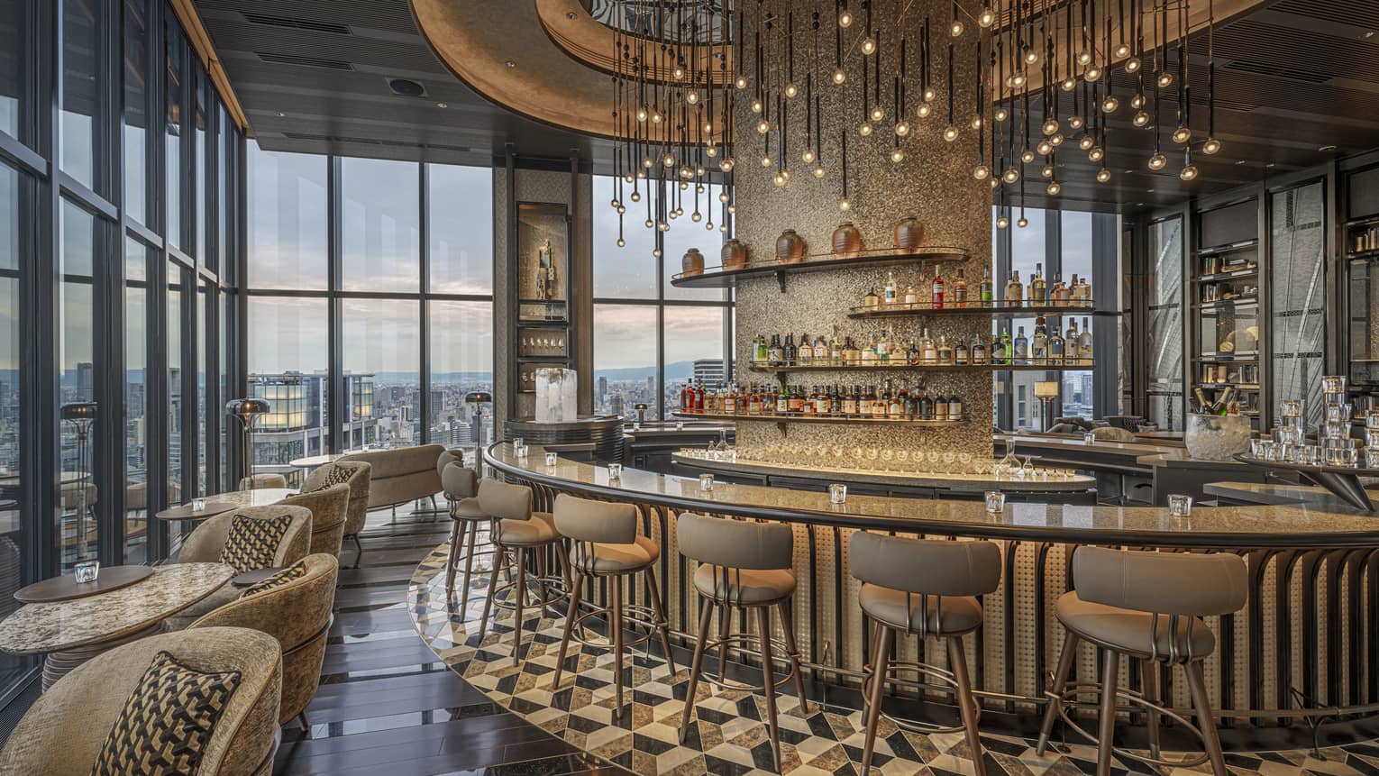 Large circular granite-topped bar in a modern luxury restaurant surrounded by a bank of windows overlooking city at dusk.
