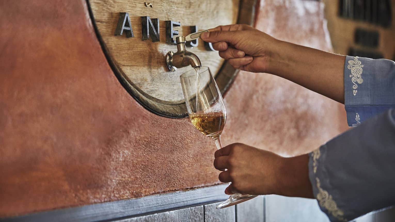 A woman pours tequila from tap into wine glass at a tequila blending experience at Four Seasons Resort Punta Mita.