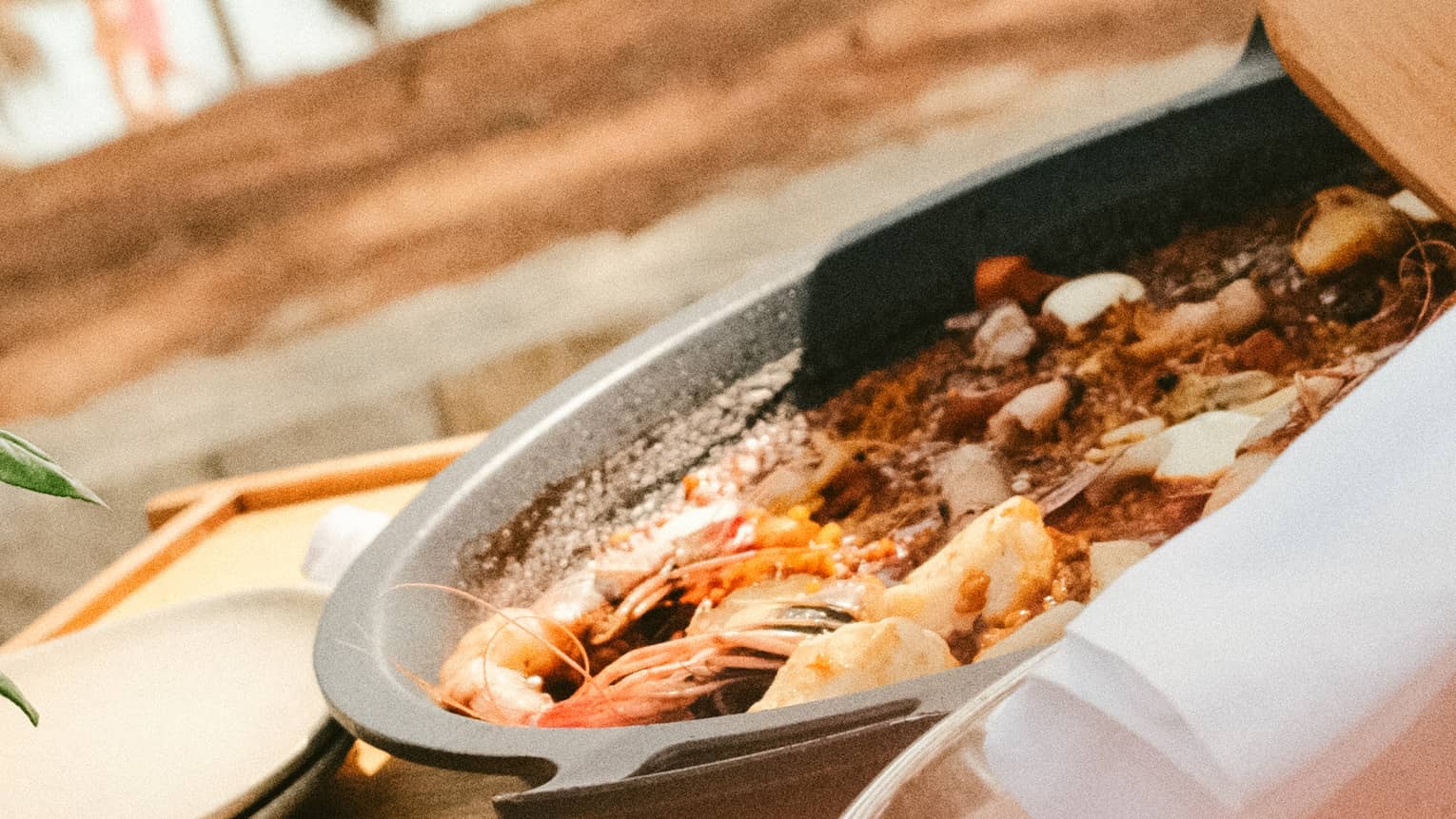 A person stirs a pan of cooked seafood with a wood spatula.