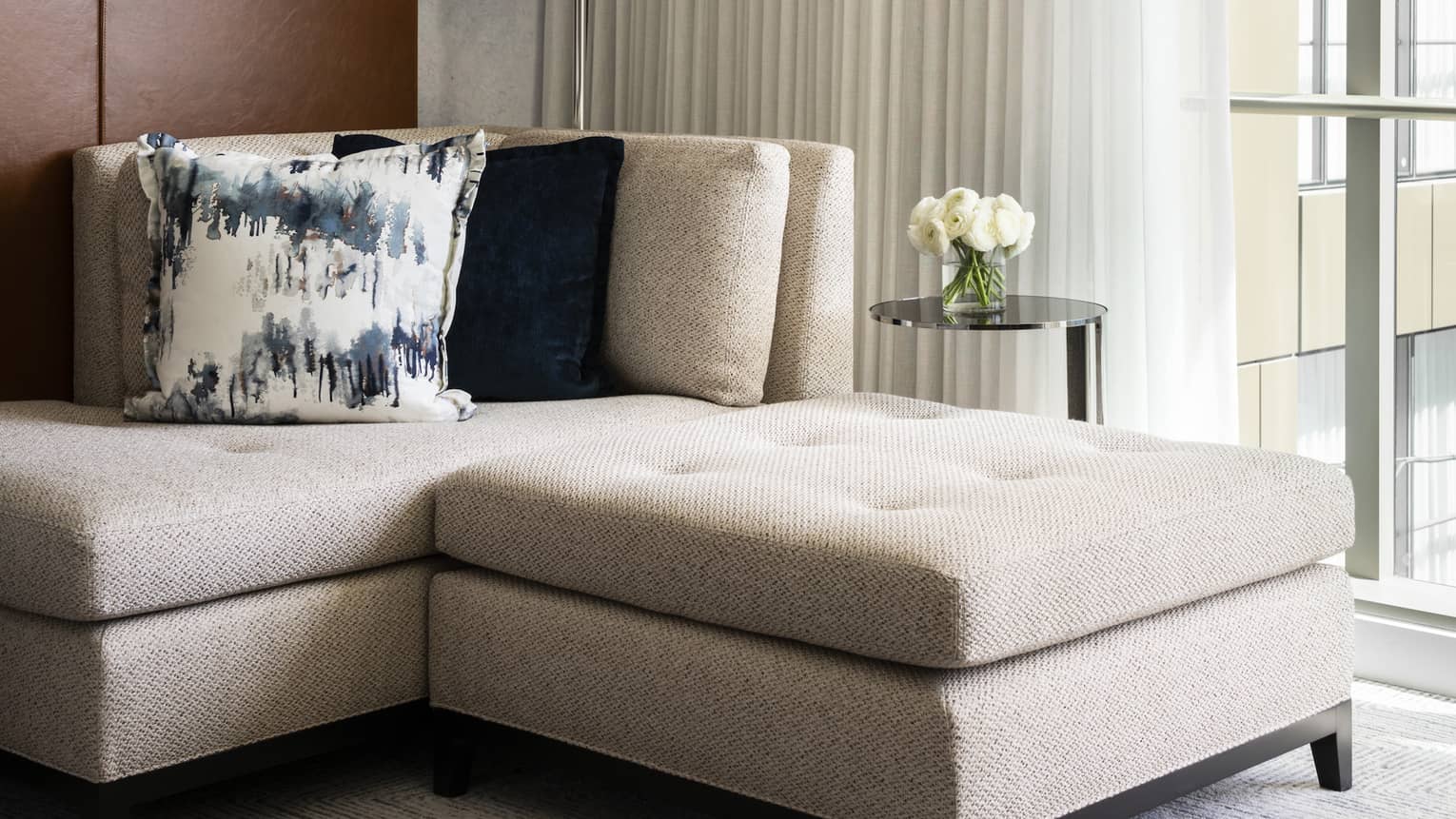 White flowers sit on a table next to a couch with plush cushions