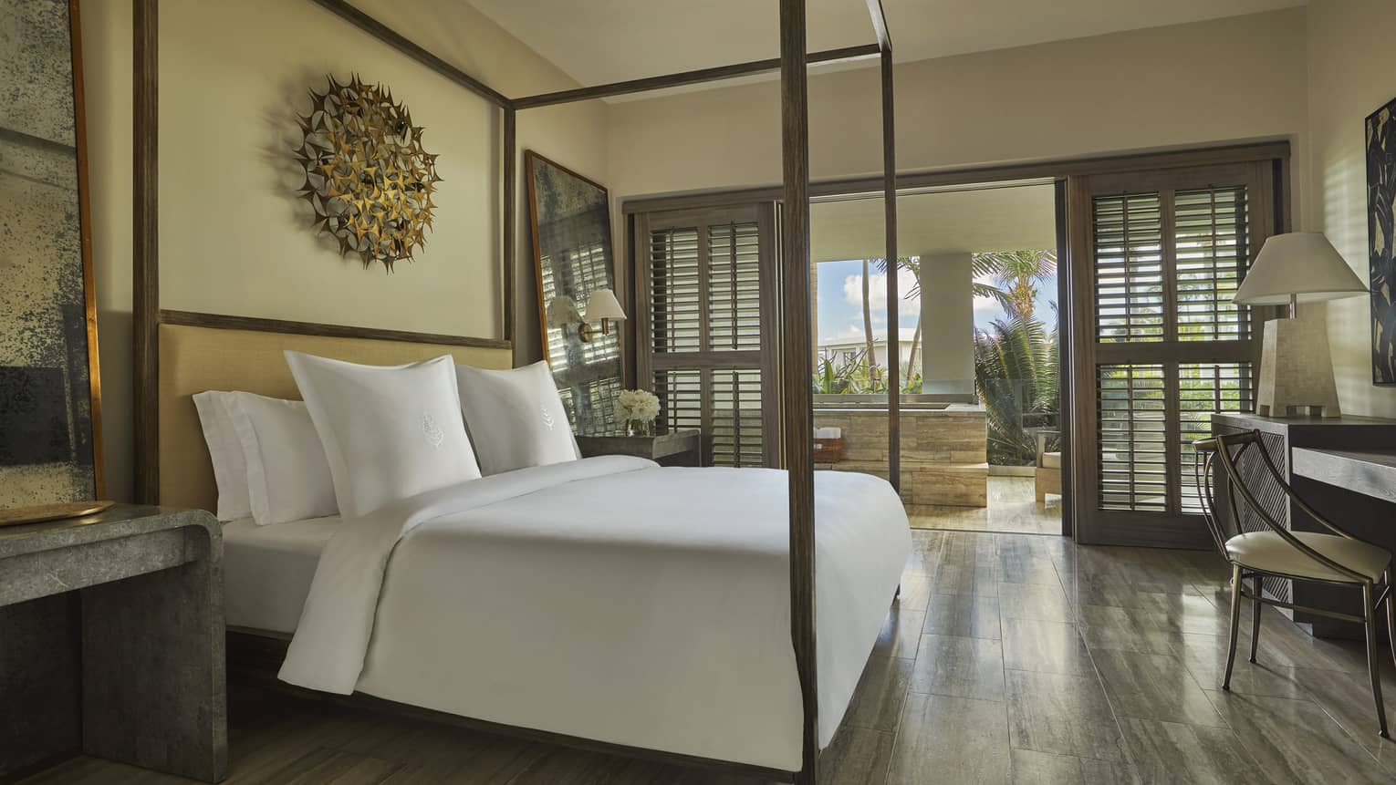 Three-bedroom penthouse bedroom, white bed with canopy frame, brass art on wall, desk, open patio door with wood shutter