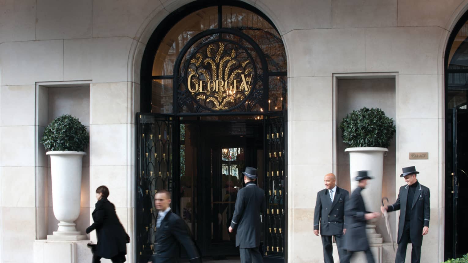 People walk quickly past doormen in hars at arched Four Seasons Hotel Paris front entrance